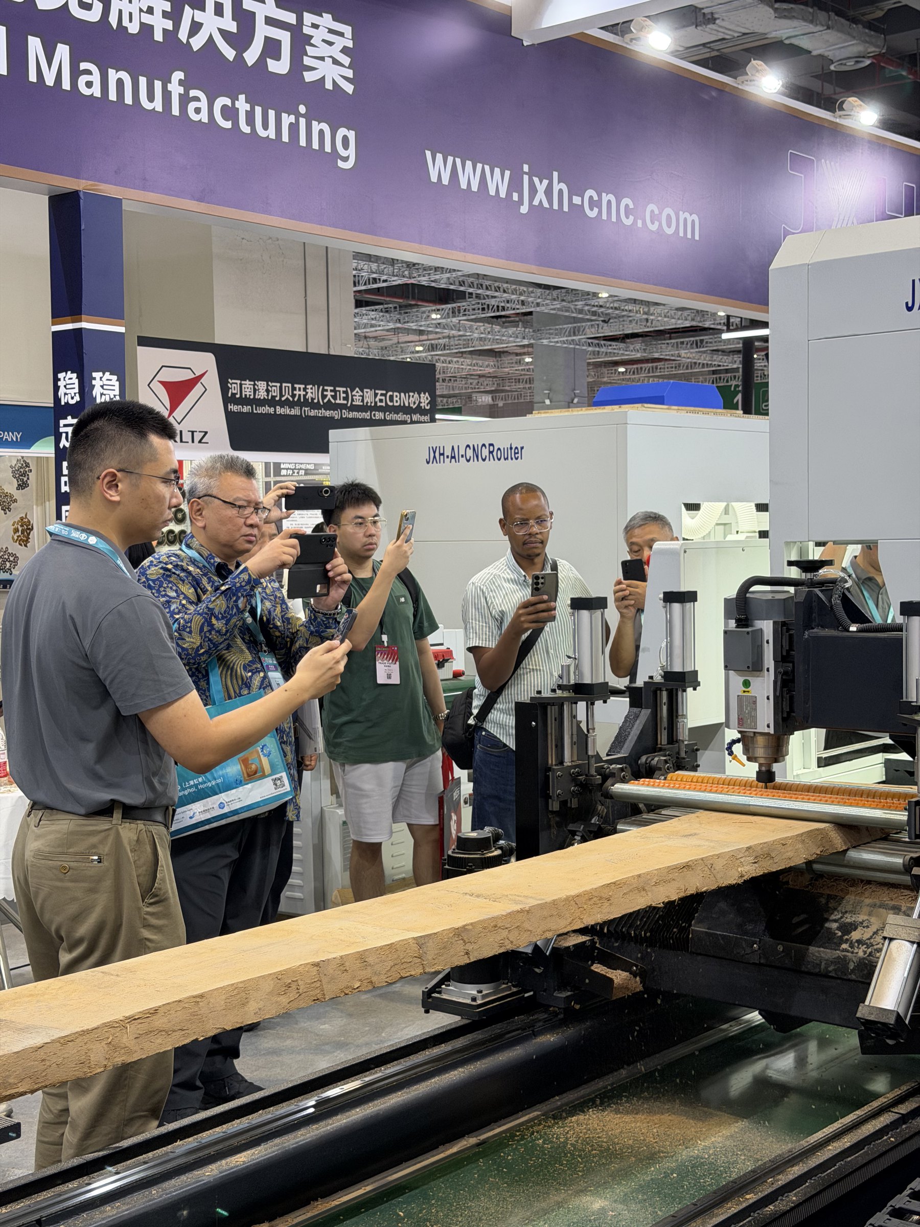 International visitors watching the JXH Dual-Station AI CNC Router process a rough board